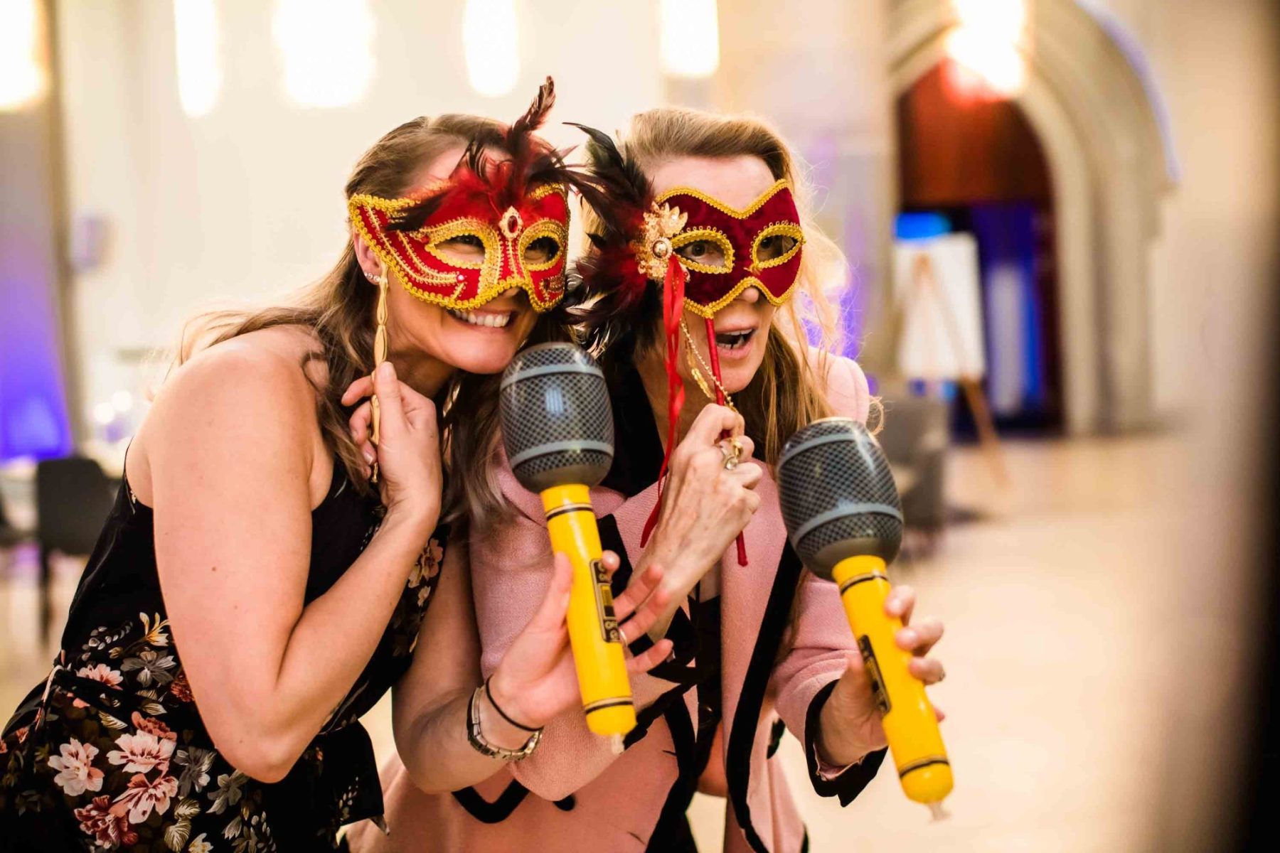 Two female wedding guests in fancy dress masks with inflatable microphones